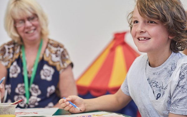 A young boy smiling while painting at school.