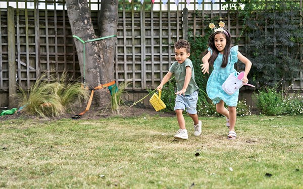Two young children smiling while hunting for Easter eggs.