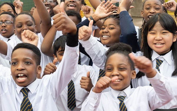A group of schoolchildren facing the camera smiling and raising their hands