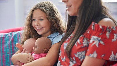 Young girl sat down with dolls smiling.