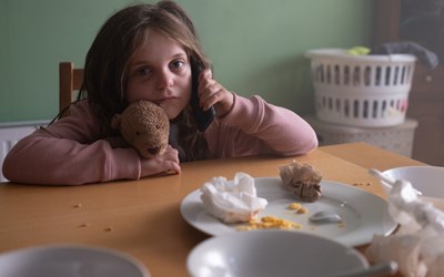 A young child making a phone call while staring blankly into the distance.