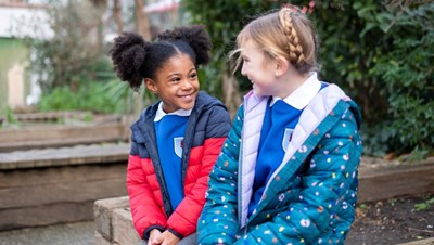 Two smiling young girls sat outside.