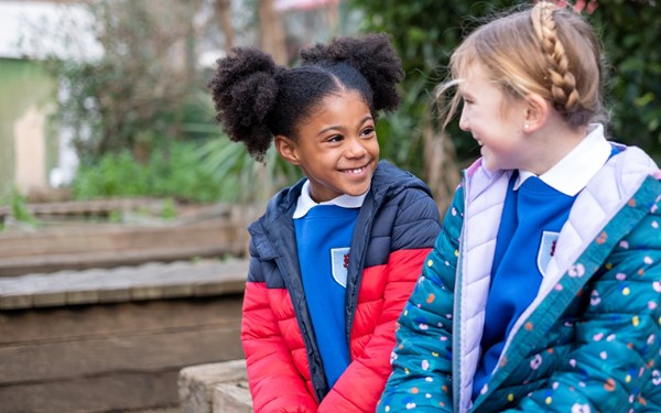 Two smiling young girls sat outside.