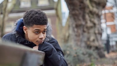 A teenage boy sat outside while staring into the distance.