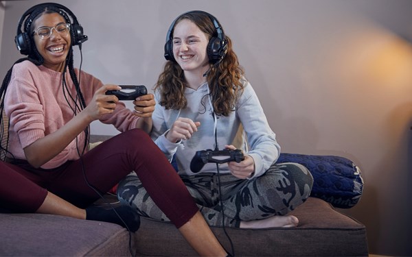 Two teenage girls playing on games consoles