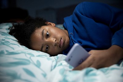 Teenage girl lay down in bed on mobile phone.