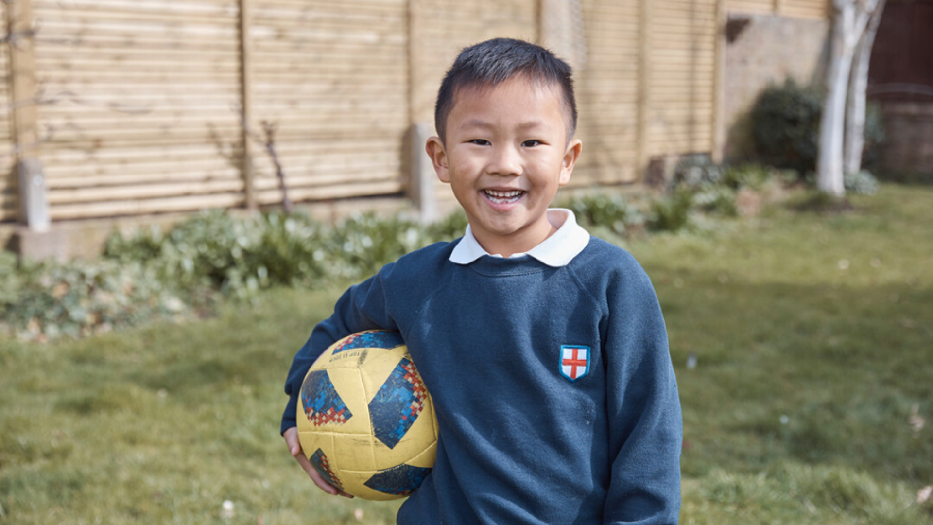 Boy holding a football in back garden