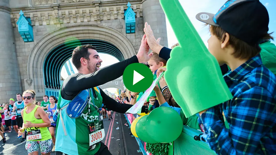 A man in a green NSPCC running vest high-fiving London Marathon spectators. A green play logo is layered onto the centre.