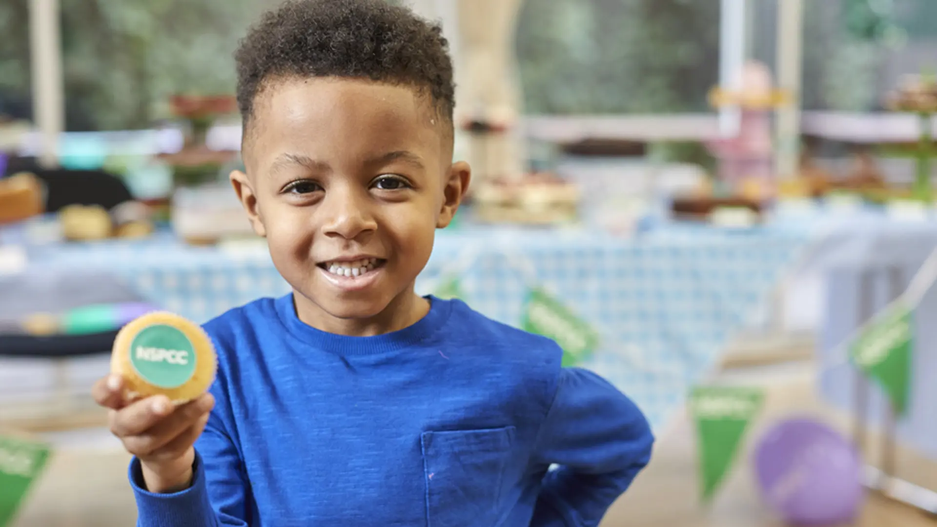 A young boy smiles and holds up a cupcake