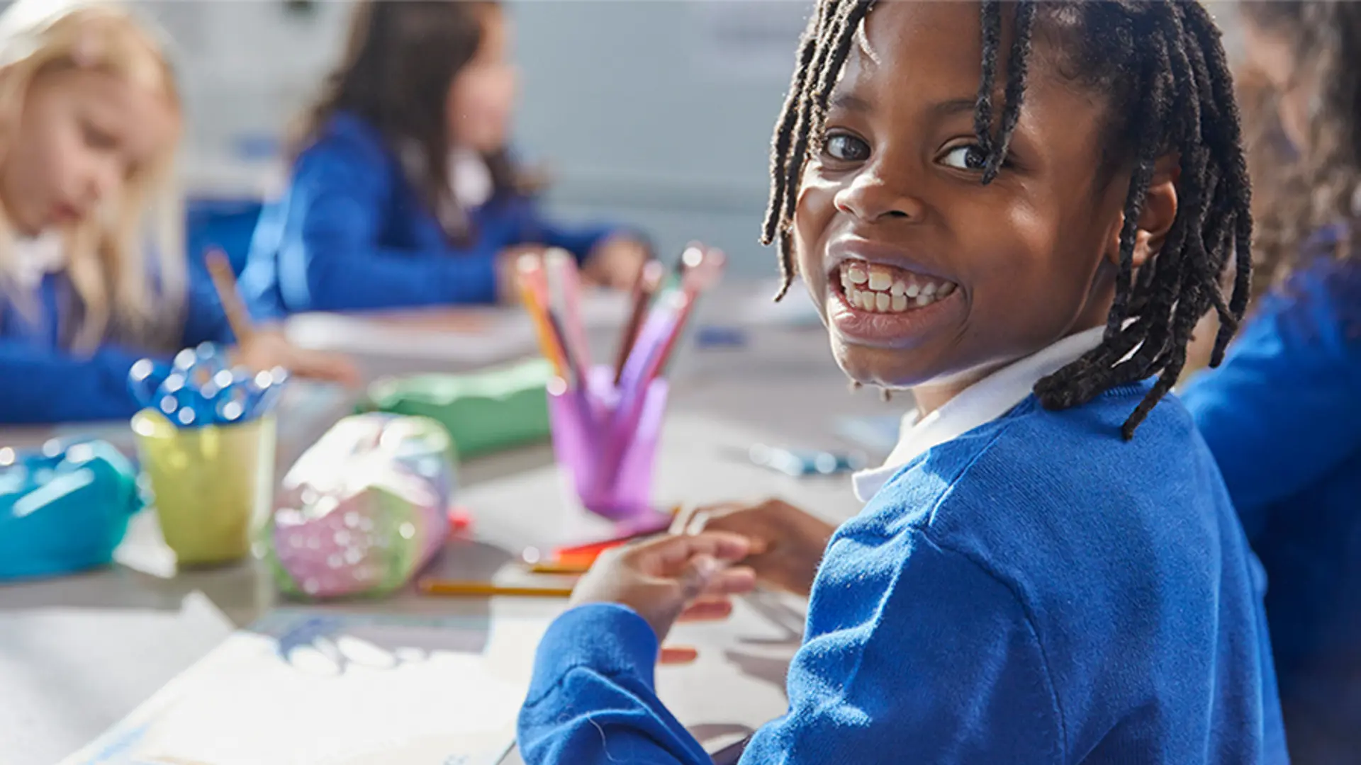 A young boy smiling while drawing at school.