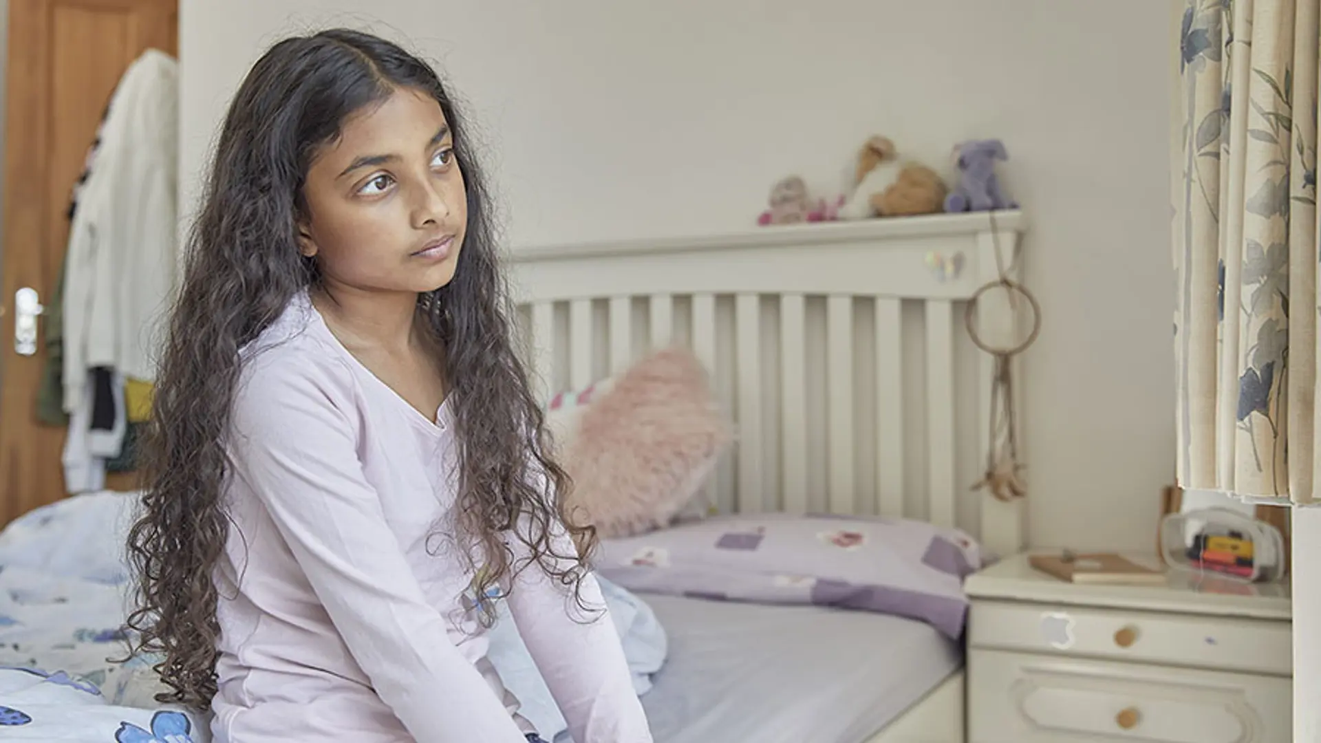 A young child sat on their bed staring blankly into the distance.