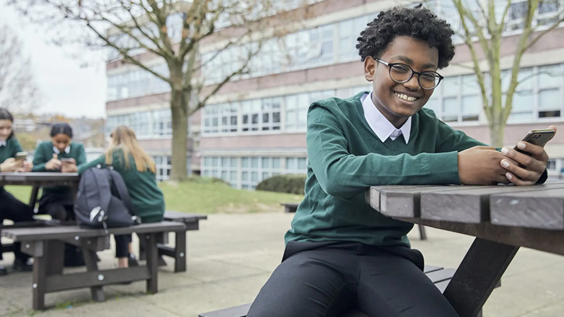 A teenager happily using a mobile phone at school.
