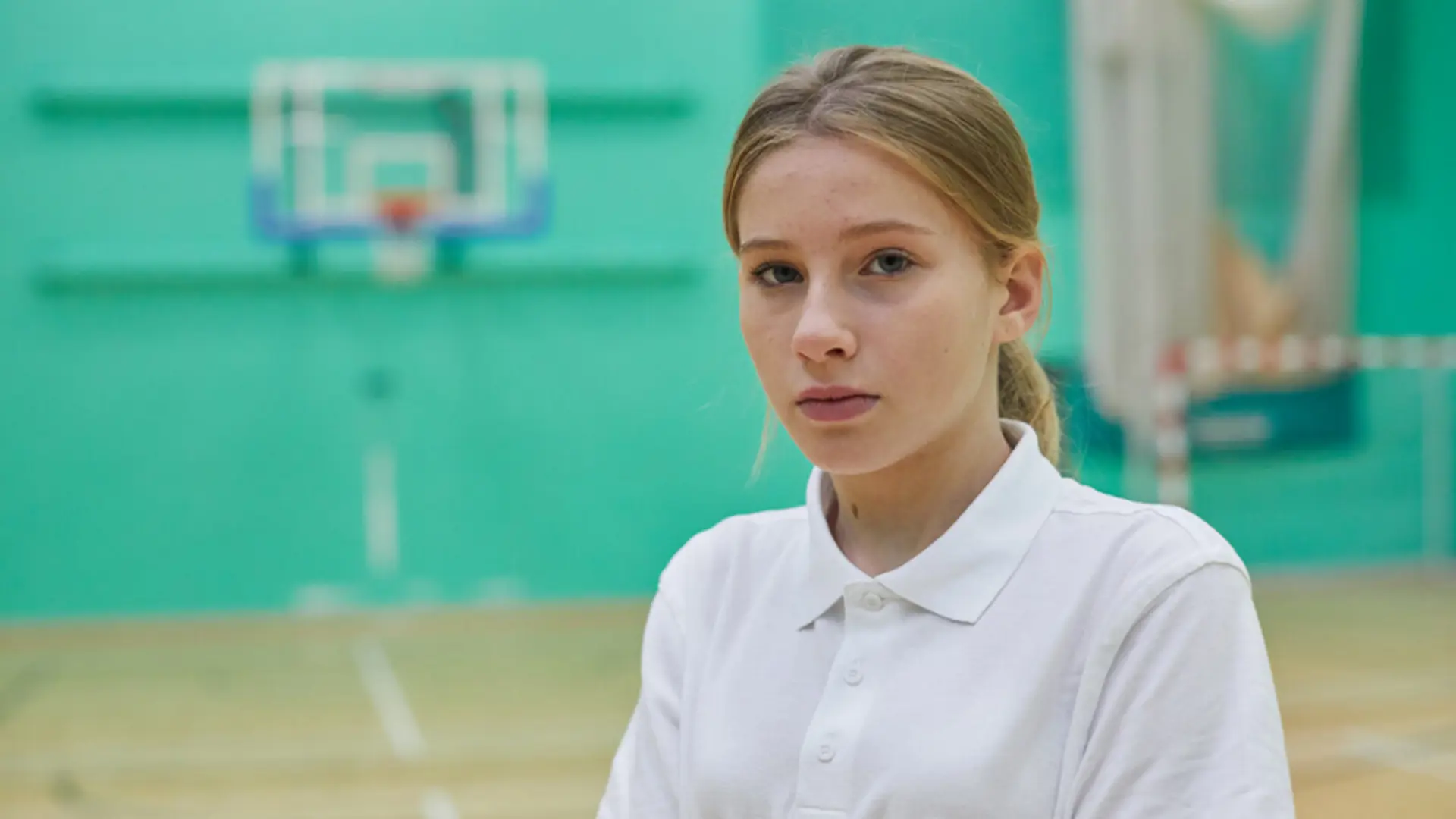Teenage girl in sports hall staring blankly into camera