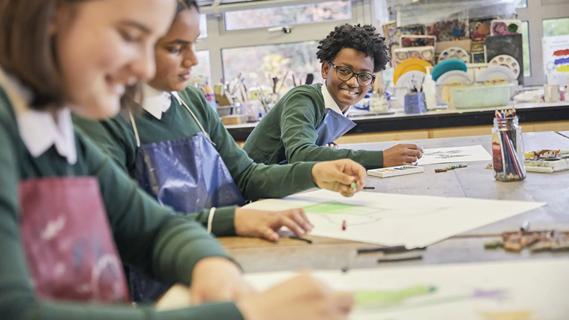 A teenage boy smiling while drawing at school.