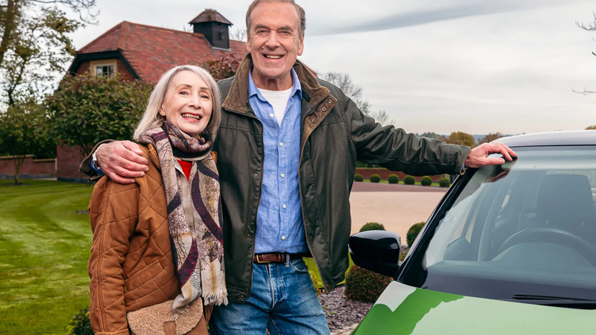 Two lottery winners smiling in front of their new car.