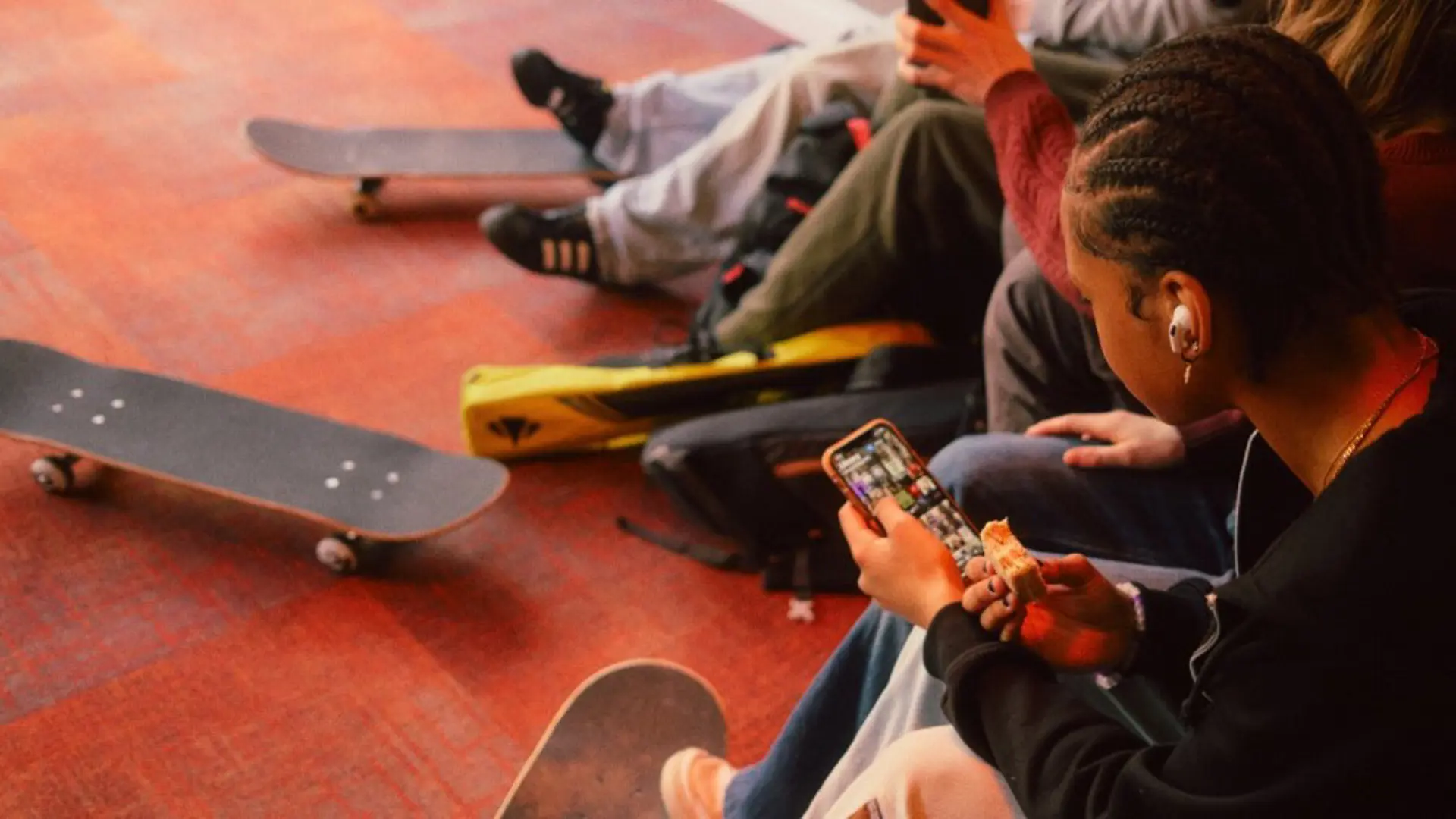 Photograph of teenagers sat inside with skateboards, using their mobile phones. 