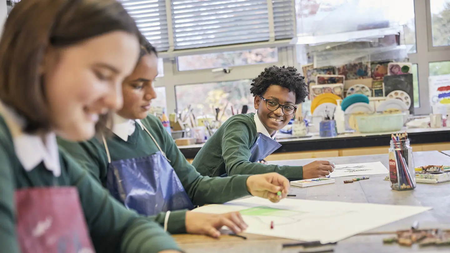 A teenage boy smiling while drawing at school.