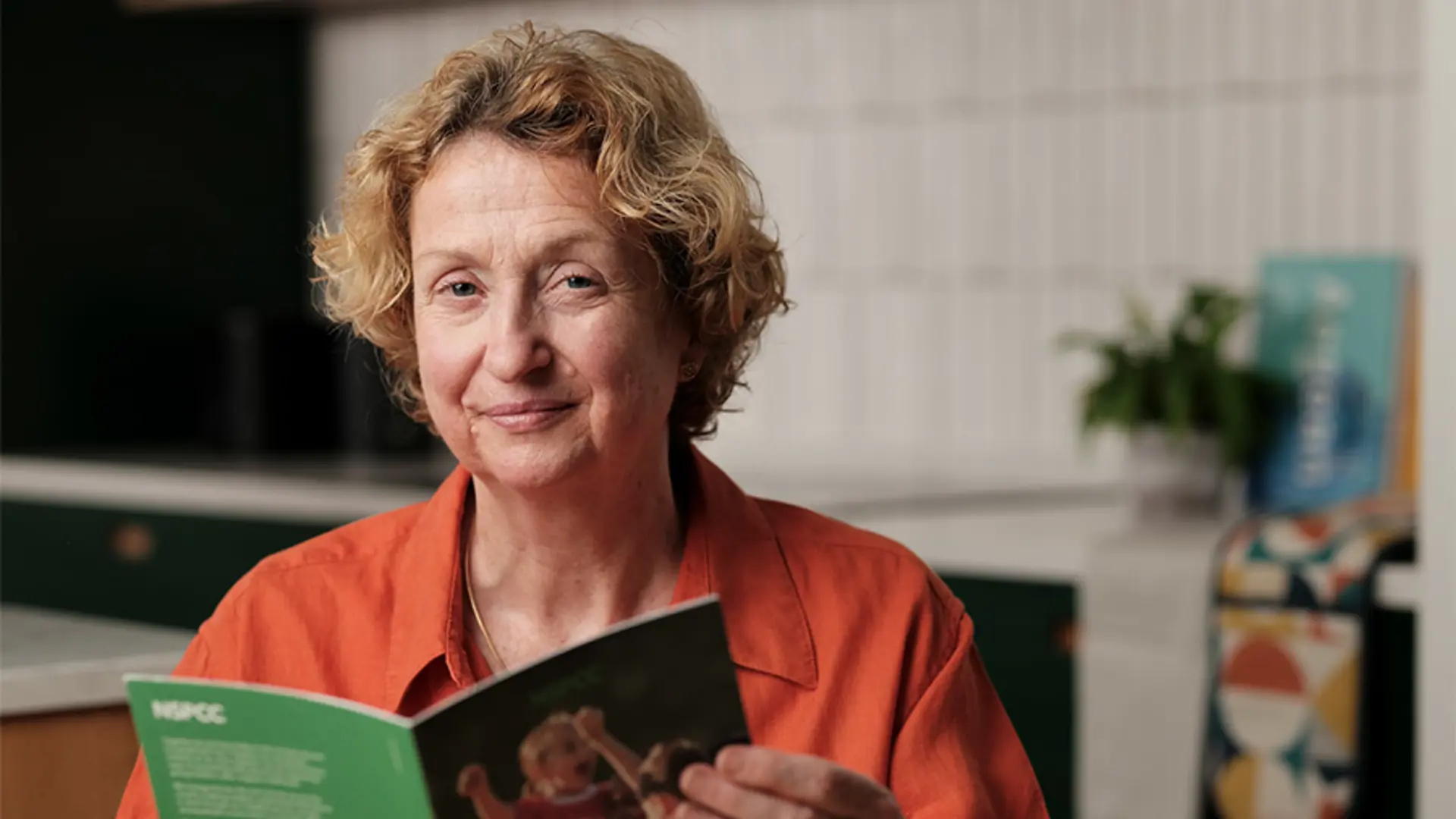 An NSPCC supporter smiling while reading a Gifts in Wills guide.