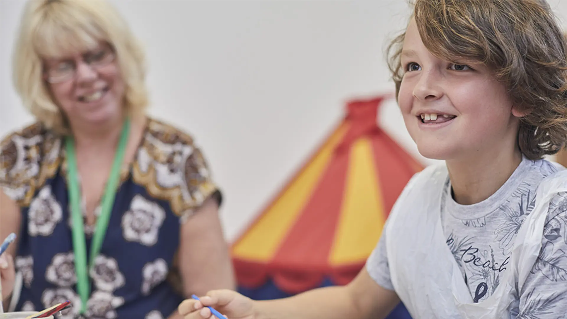 A young boy smiling while painting at school.