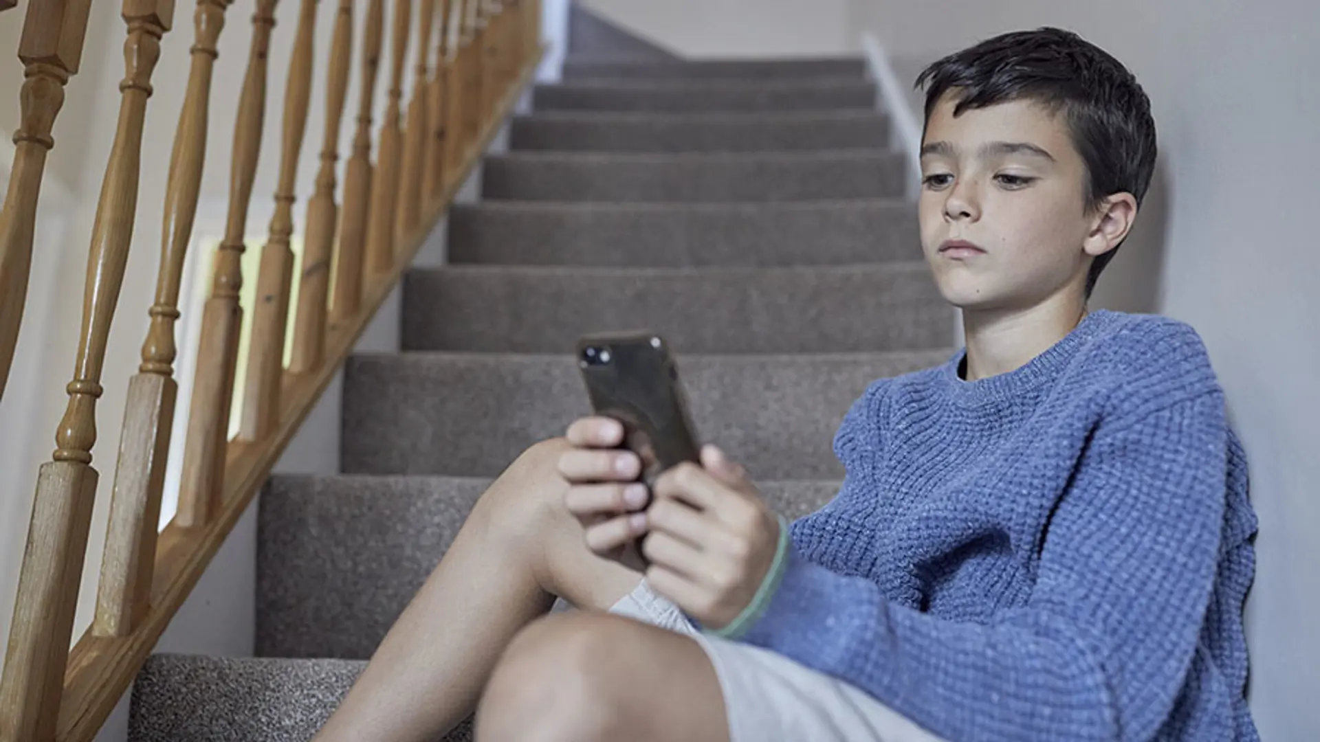 A teenager staring blankly at their mobile phone.