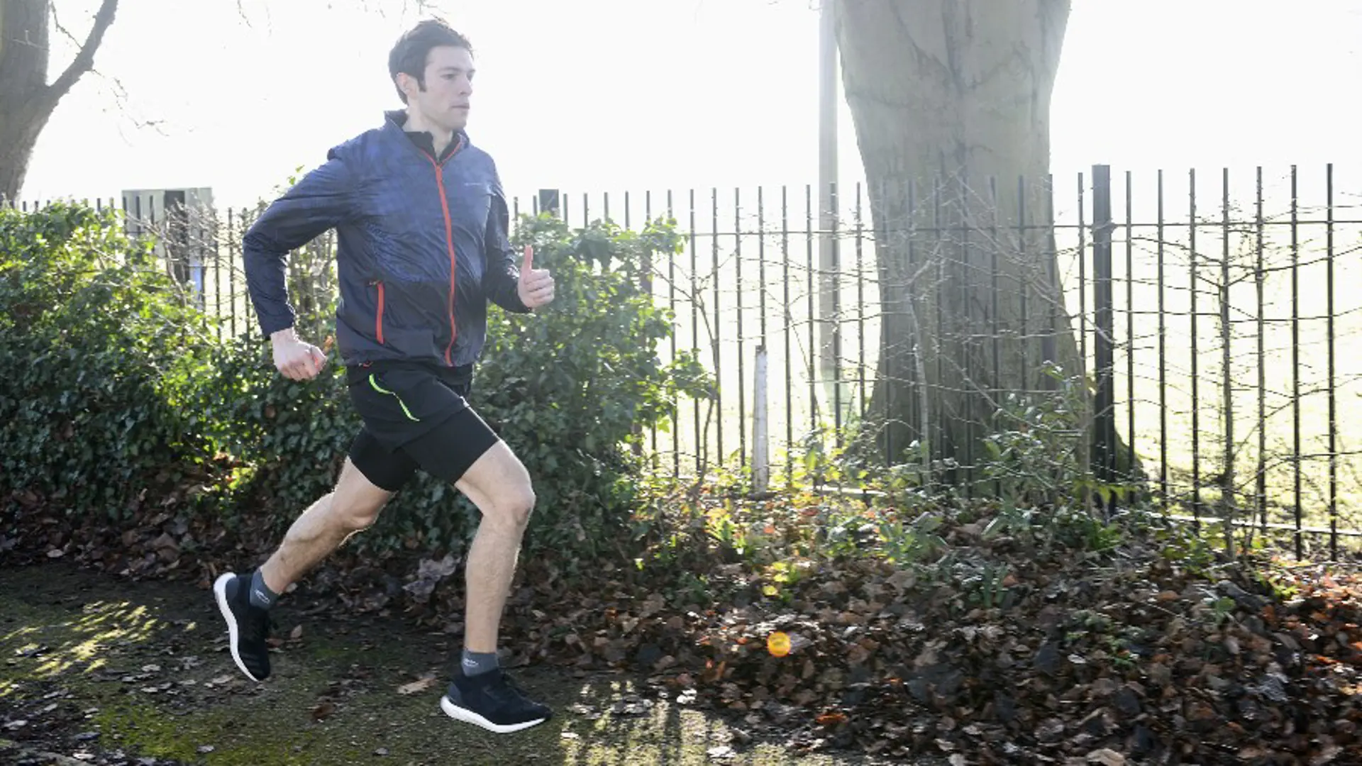 A man running through a park, wearing a waterproof jacket