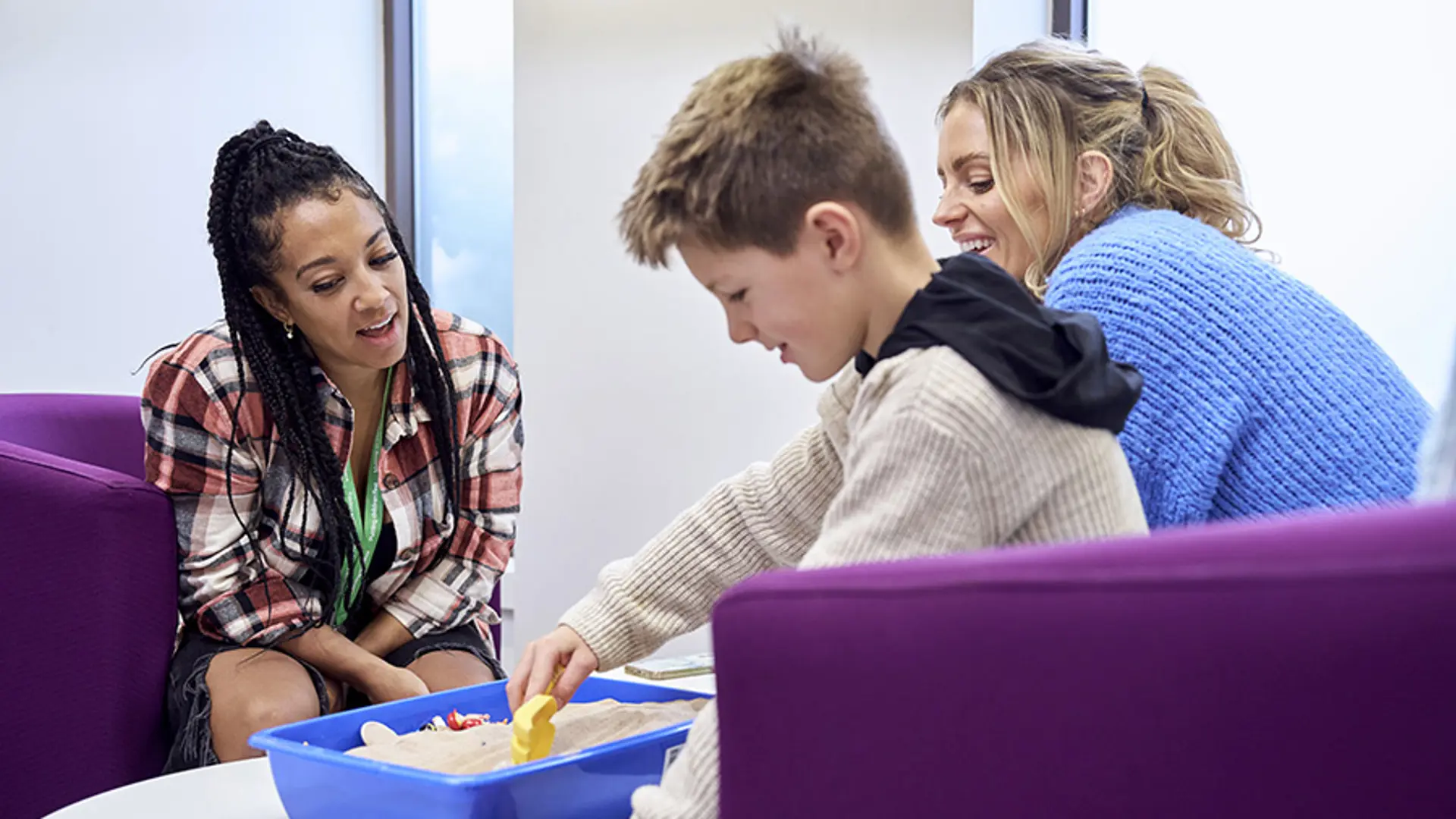 A child and their parent smiling while having a conversation with an NSPCC service practitioner.