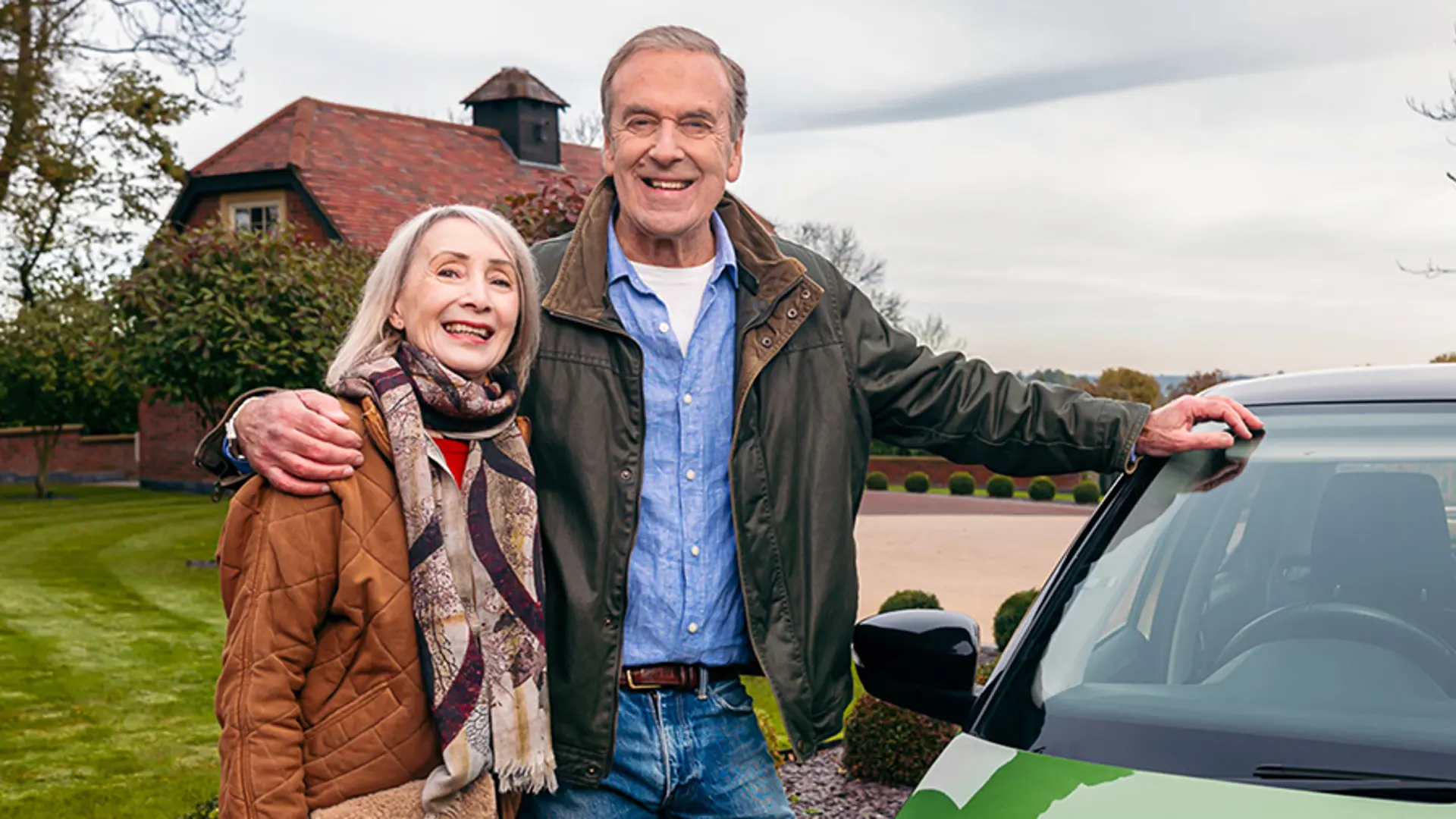 Two lottery winners smiling in front of their new car.