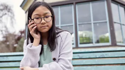 Photograph of a child sat outside making a call on their mobile phone.