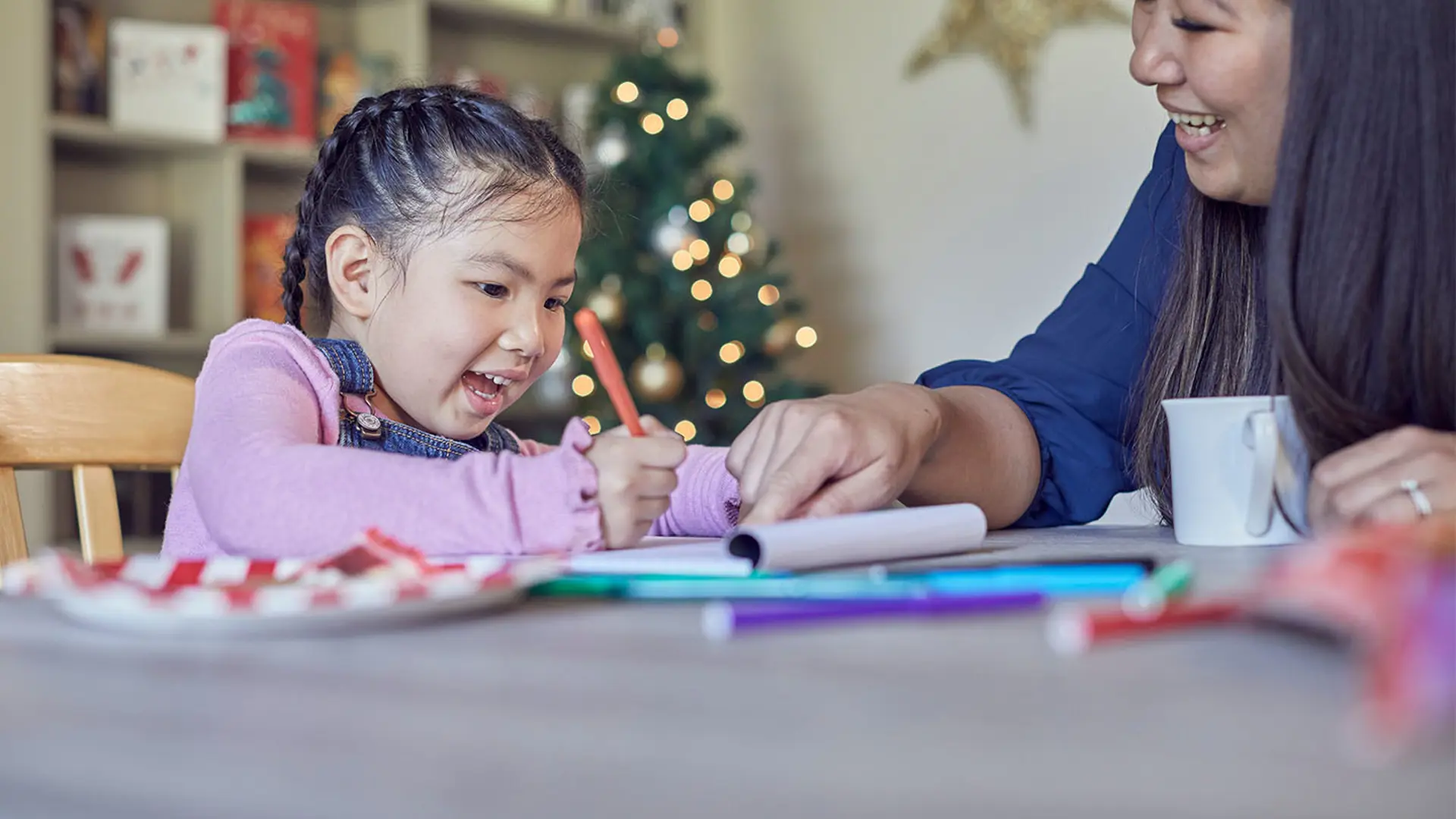 Young girl writing and smiling beside Christmas tree