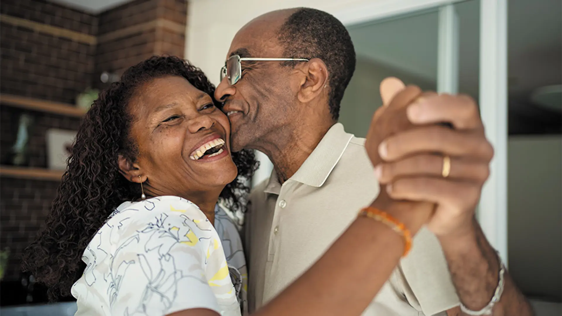 A couple laughing and smiling while dancing together in their living room.