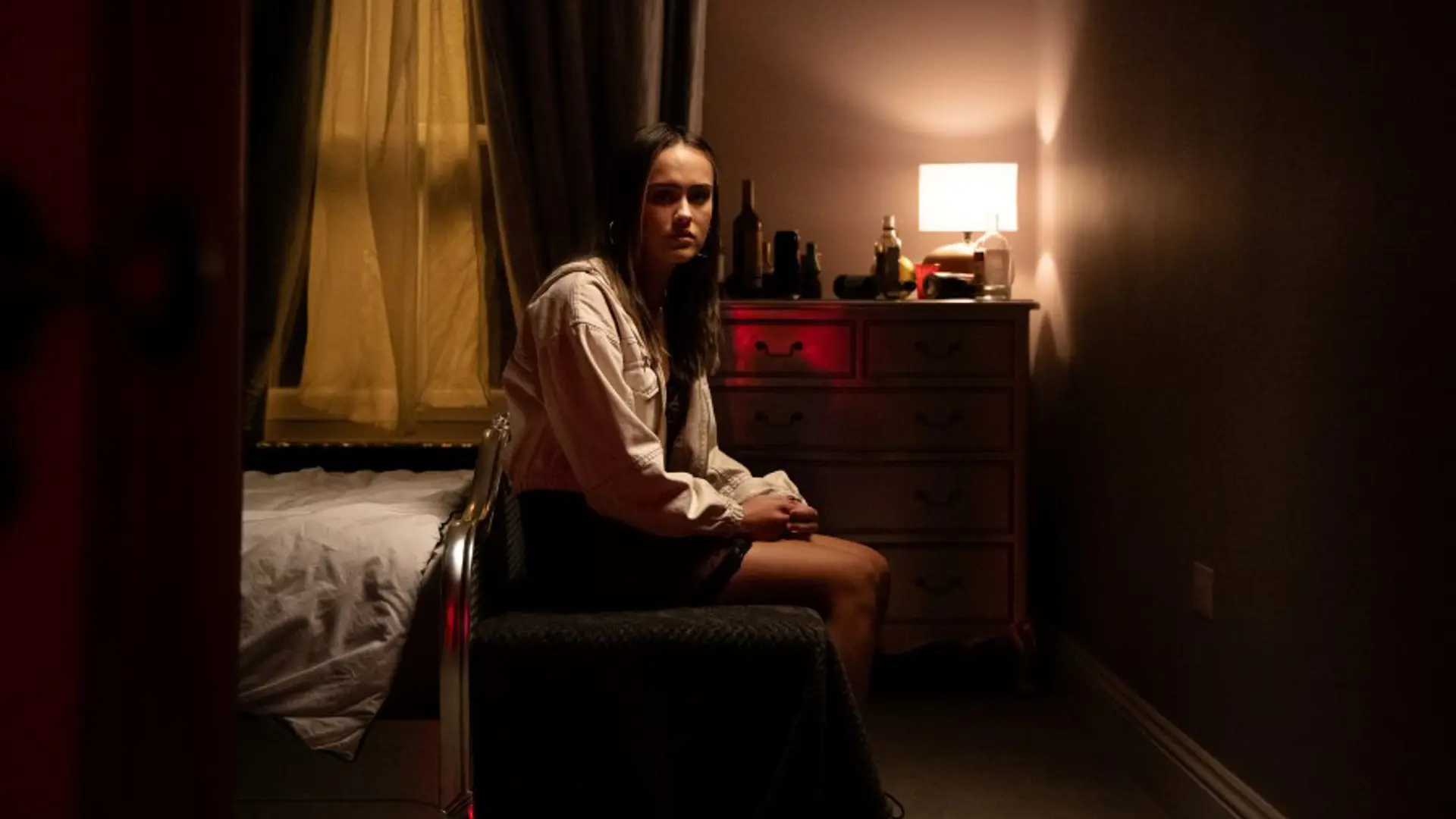 Photograph of a young person sat on a bed looking towards the door.