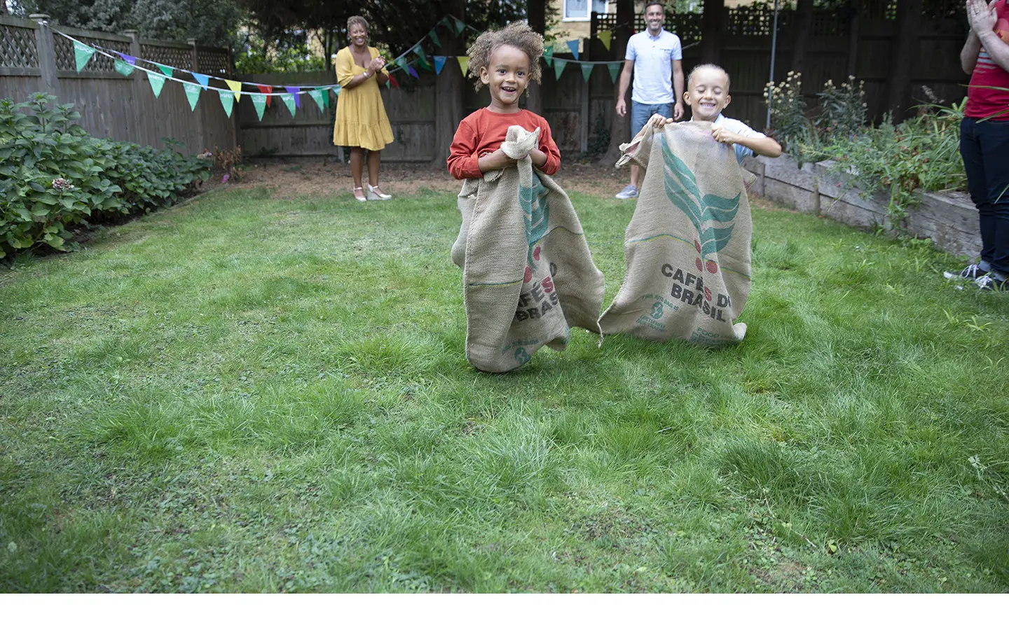 Two young children laughing and smiling while taking part in a sack race.
