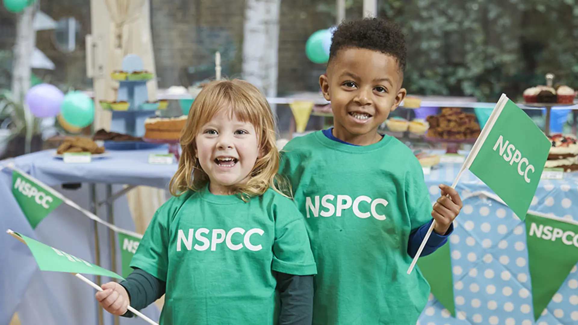 Two young children in green NSPCC t-shirts smiling at the camera.