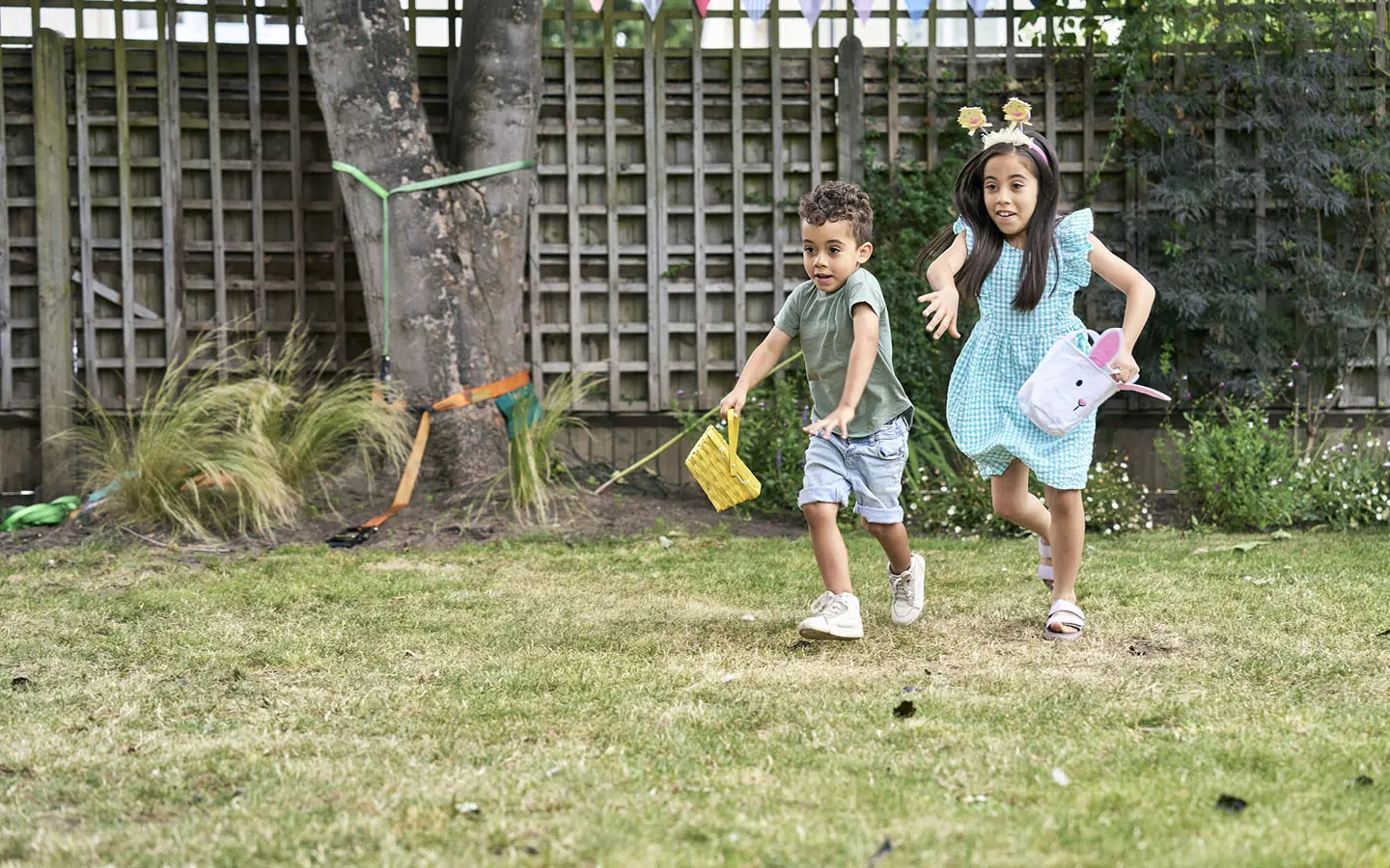 Two young children smiling while hunting for Easter eggs.