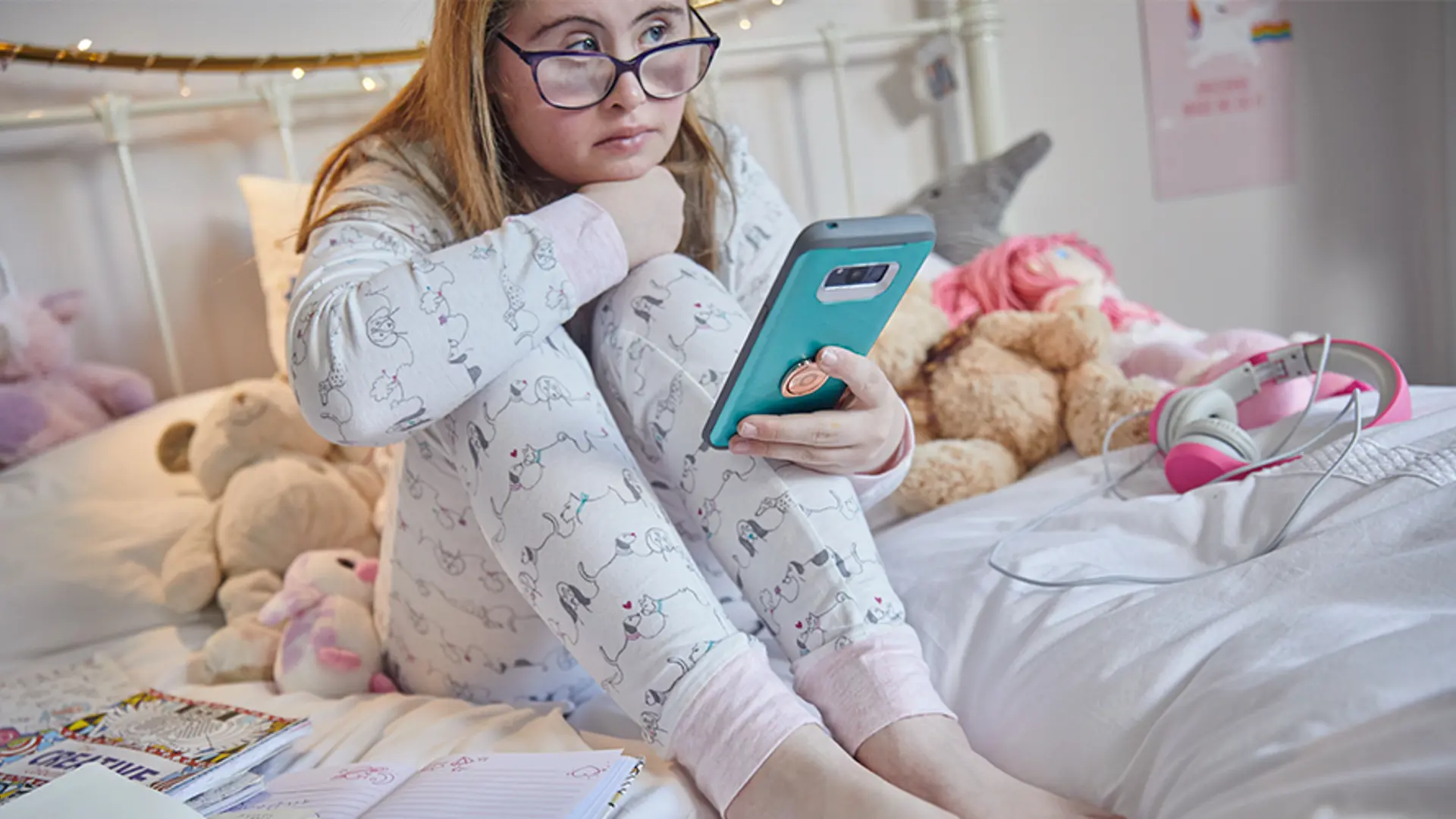 Young girl checking phone in bed surrounded by teddy bears