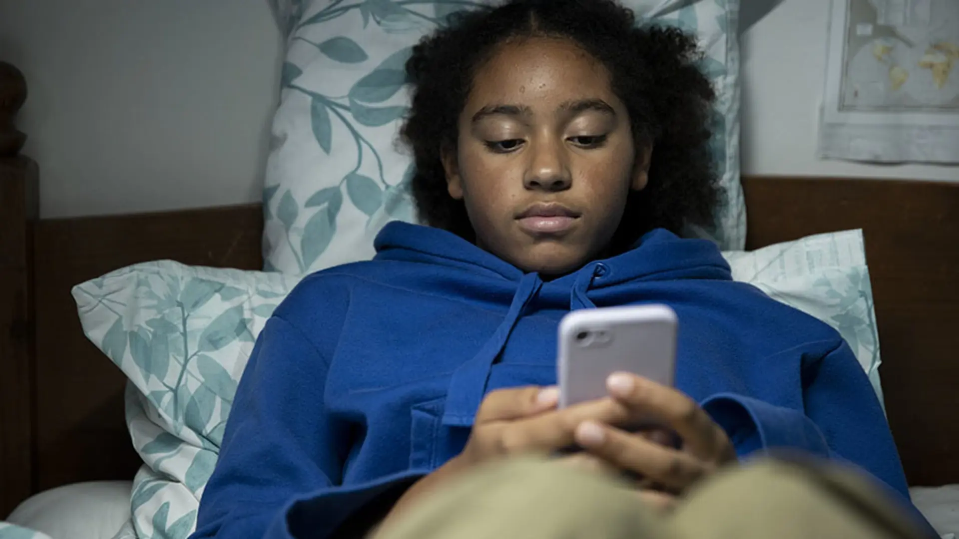 A teenager sat on their bed while using their mobile.