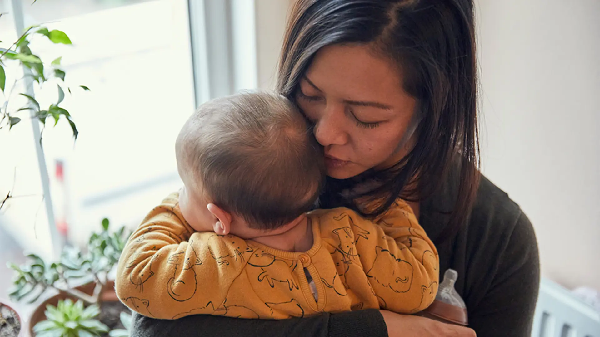 Mother suffering with perinatal mental health holds her baby close to her chest