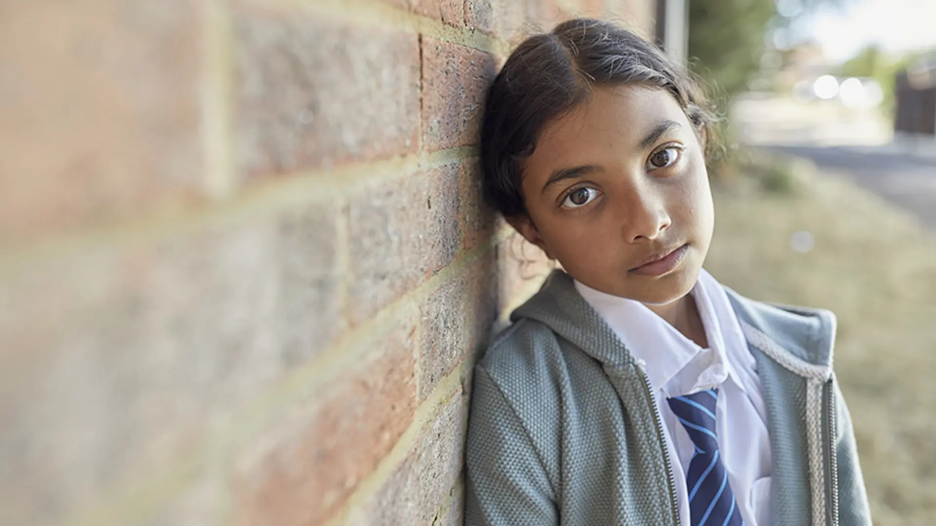 A young child stood against a brick wall while staring blankly into the camera.