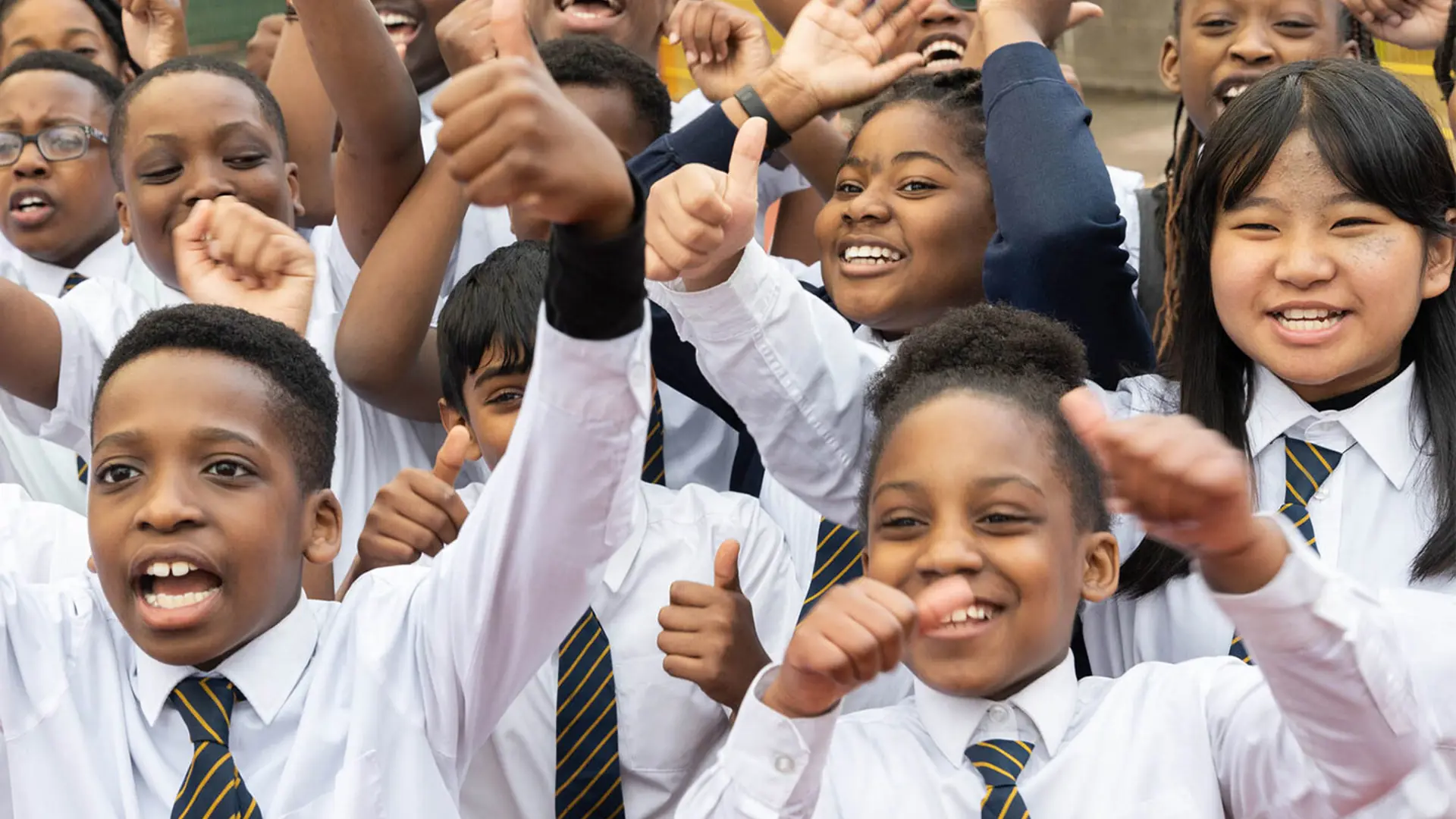 A group of schoolchildren facing the camera smiling and raising their hands