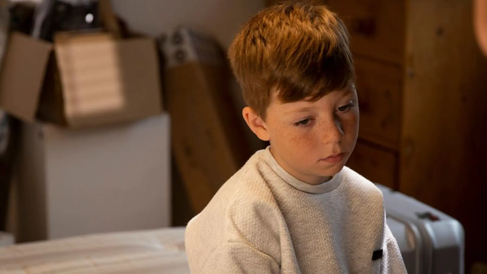 A young boy sat on his bed looking sad.