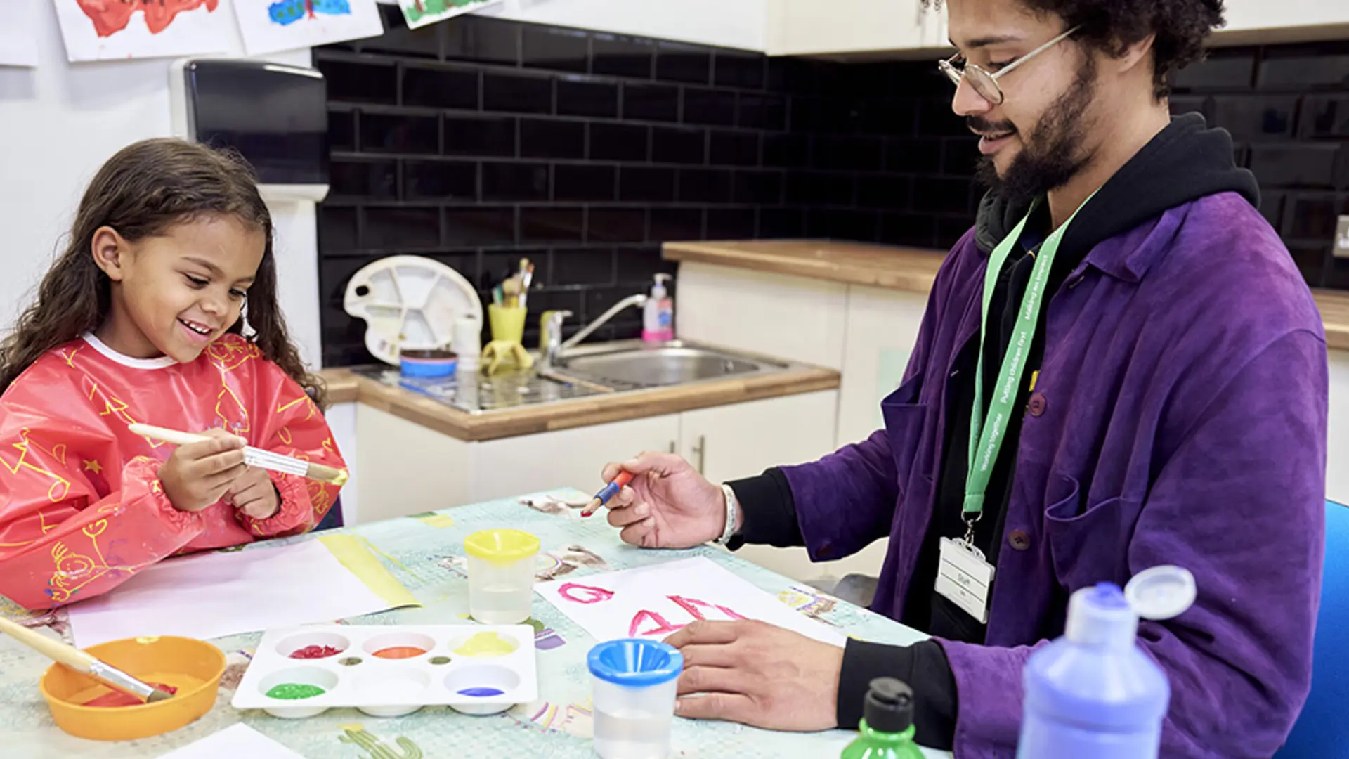 A young child smiling while painting with an NSPCC service practitioner.